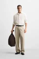 Pantalón color beige de corte ancho, con pliegues frontales, bolsillos laterales y traseros de doble vivo.