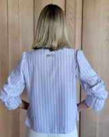Blusa color beige con cuello con volados, mangas largas abullonadas con puños elásticos y cierre con botones en la parte delantera.