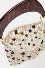 Bolso de mano tipo saca, tejido en red de color crudo, adornado con cuentas ovaladas de colores variados (rojo, negro, verde menta, beige). Posee un asa rígida de mano con acabado carey marrón oscuro.