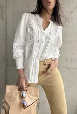 Camisa blanca de manga larga con detalles de broderie y calados en el frente y las mangas. Tiene cuello mao y cierre frontal con botones. Los puños son elásticos.