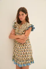 Vestido corto color crema con estampado floral en tonos azul y ocre. Tiene escote en V, mangas cortas con volados y falda con volados y terminación con guarda azul.
