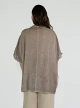 Blusa gris de lino y algodón, de corte amplio, con cuello redondo y mangas cortas con terminación desflecada. Presenta un volante diagonal en el frente.