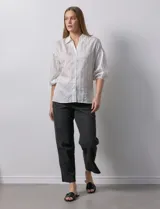 Camisa texturada blanca con líneas verticales negras, marca Hester & Orchard. Cuello a la base, escote en V y abertura central con botones. Manga ¾ con terminación fruncida.