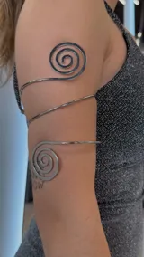 Brazalete plateado para el brazo, con diseño de espirales en los extremos.