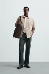 Sobrecamisa negra de tejido con elasticidad, cuello solapa y manga corta. Tiene dos bolsillos de plastrón en el pecho y cierre frontal con botones a presión.