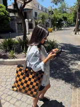 Bolso tote de cuero trenzado a mano, forrado por dentro. Presenta un patrón de cuadros grandes en tonos marrón oscuro y celeste/azul claro.