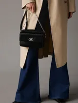 Bandolera negra con monograma CK grabado en toda la superficie. Tiene correa de cadena plateada, cierre superior con cremallera, bolsillo frontal con cierre giratorio y herrajes plateados.