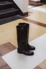 Bota alta de cuero color marrón, con caña recta y suela plana.