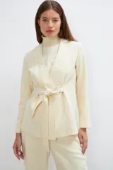 Chaqueta corta color beige, entallada, con escote en V, manga larga y cierre frontal con lazo fijo. Confeccionada en lana fina sin teñir, con bolsillos escondidos y terminaciones enviadas. Hecha 100% en Uruguay.