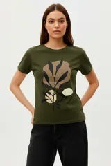 Remera de algodón color verde militar, manga corta y cuello redondo, con un estampado abstracto de hojas y formas en tonos beige, marrón y negro.