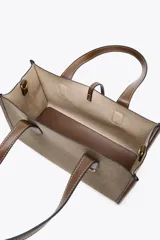 Bolso tipo shopper color marrón con doble asa corta y correa larga extraíble. Tiene detalle de pespuntes y anilla metálica decorativa. Incluye bolsa de tela interior extraíble con cierre fruncido.