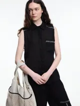 Camisa sin mangas negra de lino con cuello clásico, cierre frontal abotonado y bolsillo de parche en el pecho. Presenta bordados tipo pespunte en contraste en el frente y canesú trasero.