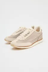 Zapatillas deportivas tipo running, color gris claro con detalles en beige y blanco. Combinación de materiales en el corte y suela en contraste. Cierre mediante cordones de color.