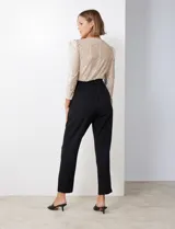 Enterito de fiesta con torso de lentejuelas color champagne, escote en V cruzado, mangas 3/4 con frunces en los hombros, cintura elastizada con lazo negro y pantalón negro de corte recto con bolsillos laterales.