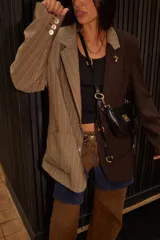 Blazer oversize con diseño asimétrico, mitad en tela a cuadros gris y blanco, mitad en tela lisa gris. Tiene solapas, cierre con botones y pin de salchicha decorativo.