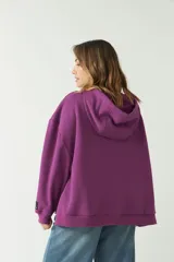 Buzo canguro verde con corte recto y amplio, capucha con cordones regulables y bolsillo frontal con cierre.