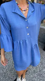 Vestido corto de manga larga con volados, color lavanda, con cuello camisero y botones frontales.