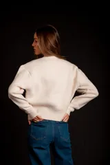 Buzo gris de punto con cuello redondo, mangas largas abullonadas y cierre frontal asimétrico.