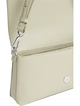 Cartera de hombro color crema, marca Calvin Klein, modelo CK Must. Tiene correa de hombro ajustable con el logo de la marca y otra correa más fina.