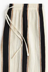 Pantalón de punto color crema con rayas verticales negras y marrones, de corte holgado y tiro alto, con cintura elástica y cordón ajustable.