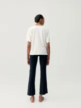 Camiseta holgada de manga corta, color blanco roto, con cuello redondo y un estampado sutil de letras en tono gris claro.