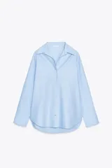 Camisa celeste de corte clásico, con cuello solapa, manga larga, bajo asimétrico y cierre frontal con botones.