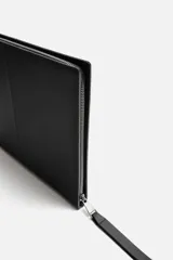 Bolso tipo sobre negro de cuero, con costura central y asa de mano. Cierre con cremallera y compartimentos interiores.