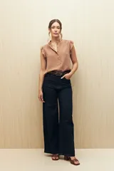 Camisa color beige con textura suave, cuello mao con volado y mangas cortas con pequeño volado. Presenta botonadura frontal.