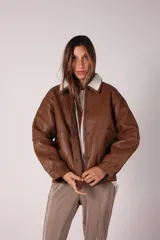 Campera bomber marrón de cuero sintético con cuello de corderito blanco, cierre con botones a presión, bolsillos delanteros con solapa y puños y cintura elastizados.