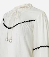 Blusa color crema de tricolina con detalles de ondas negras en cuello, mangas y frente. Tiene mangas 3/4 con volados y lazo en el cuello.