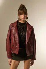 Campera estilo biker de eco-cuero color bordó, con cuello solapa ancho, manga larga y calce holgado. Presenta cierre frontal y botones decorativos en la parte inferior delantera.