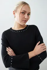 Remera negra de manga larga con cuello redondo y tachas plateadas en el cuello y los puños.