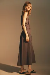 Vestido midi marrón sin mangas, con cuello solapa, escote en pico, cierre frontal con botones y cinturón de la misma tela con hebilla metálica.