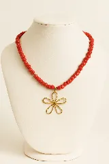 Collar corto de cuentas redondas de nácar rojo con dije de flor dorada.