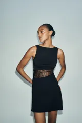 Vestido corto negro de cuello barco y sin mangas, con panel lateral de encaje floral transparente.