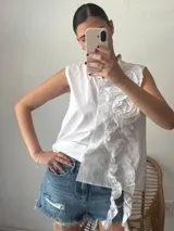 Camisa blanca sin mangas con cuello mao y volados en el frente.