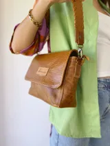 Bandolera color camel de cuero con forro de tela, correa corta con tientos y bolsillo interno.