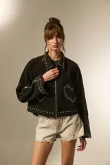 Campera cropped de jean color negro, con cuello camisero, cierre frontal y detalles de tachas plateadas en el cuello, hombros, mangas y ruedo. Presenta un diseño de tachas en forma de corazón en el pecho.