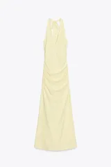 Vestido largo color amarillo pálido, con cuello halter que se ata en la nuca, escote en pico y frunces laterales.