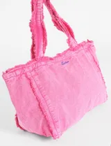 Bolso tote de tela color rosa vibrante con efecto lavado. Presenta bordes y costuras desflecadas y un pequeño bordado en hilo azul en el frente.