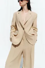 Pantalón color beige de lino, de tiro alto, con pinzas delanteras, bolsillos frontales y pernera ancha.