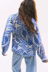 Blusa oversized con cuello elevado fruncido, abertura en V adelante y bajo recto. Mangas globo largas de corte raglán con abertura y botón en los puños. Estampado floral en tonos azules y blancos.