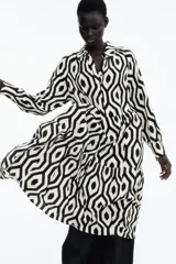 Vestido camisero midi de viscosa con estampado geométrico en blanco y negro. Tiene cuello camisero, tapeta de botones oculta, mangas largas raglán con puños sencillos y costuras fruncidas en la falda. Sin forrar.