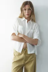 Camisa azul de cuello solapa y manga corta con dobladillo. Tiene dos bolsillos de parche en el pecho, bajo asimétrico con aberturas laterales y cierre frontal con botones ocultos.