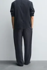 Pantalón negro de corte relajado con cintura elástica ajustable y pliegues en la parte delantera. Presenta bolsillos laterales y bolsillos traseros de parche.