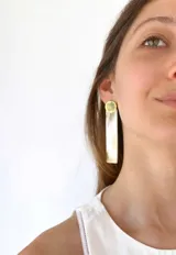Aros colgantes con base circular dorada y pieza rectangular alargada color crema.