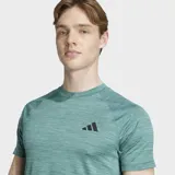 Remera de entrenamiento Adidas de corte ajustado, color verde jaspeado, con cuello redondo y mangas raglán. Presenta el logo de Adidas Badge of Sport en negro en el pecho.