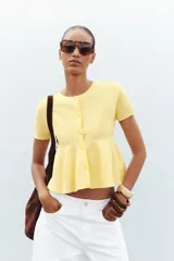 Chaqueta color amarillo claro de tejido de punto, con cuello redondo, manga corta, corte peplum y cierre frontal con botones.