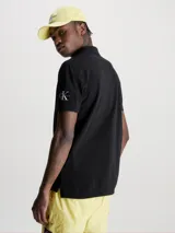 Chomba negra de piqué de algodón peinado, corte regular, cuello clásico con dos botones, mangas cortas, dobladillo con aberturas laterales y logo de Calvin Klein en la manga.