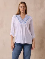 Blusa blanca de poliéster y rayón con escote en V bordado y mangas tres cuartos regulables con presilla y botón.